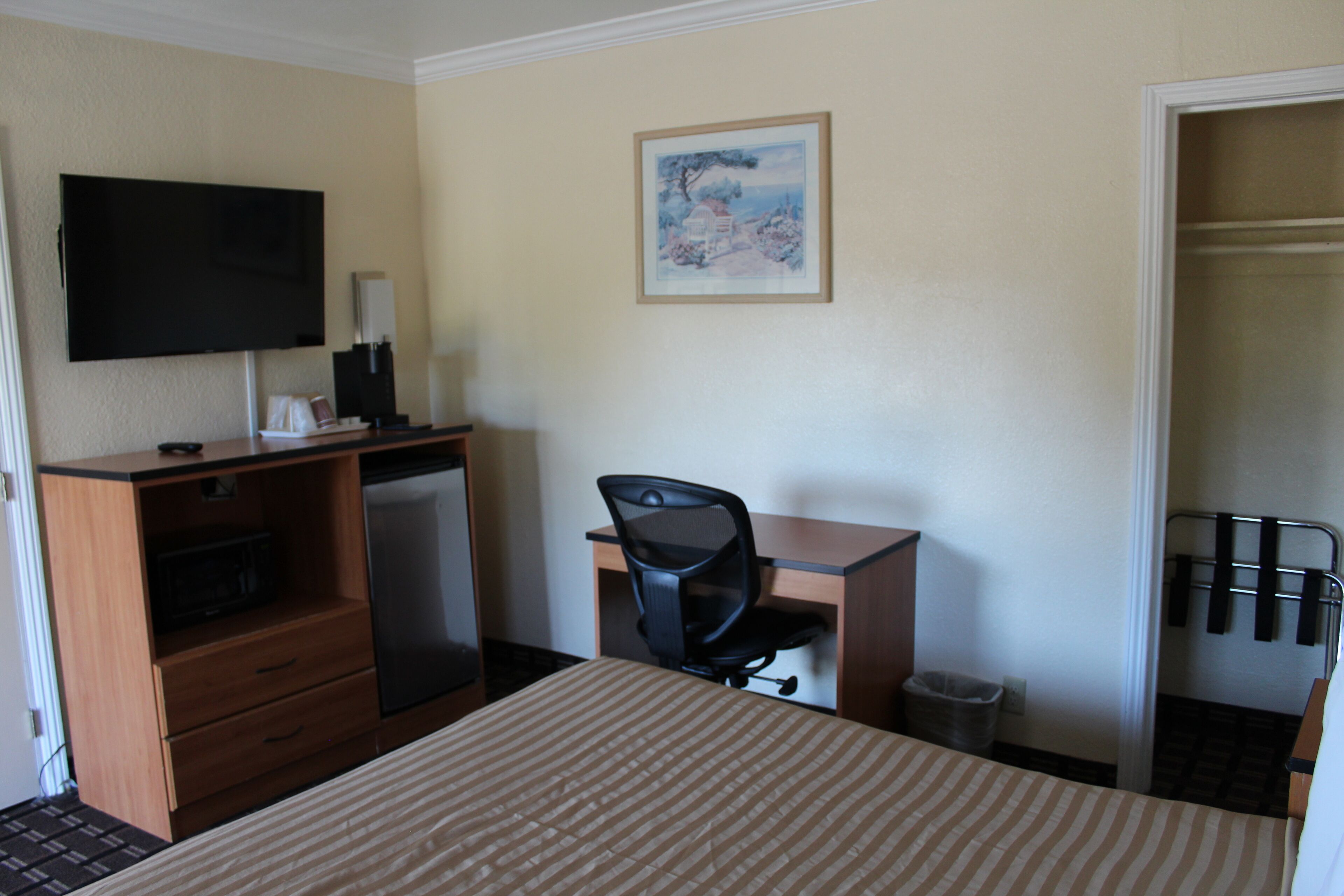 Habitación de hotel con cama, escritorio, silla, televisor y un cuadro en la pared.
