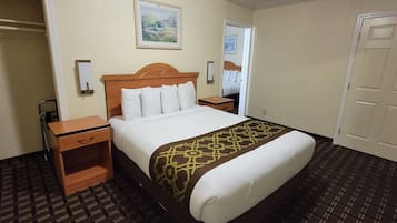 Une chambre d’hôtel avec un lit, une table de chevet en bois, une petite table, une lampe fixée au mur et une porte.