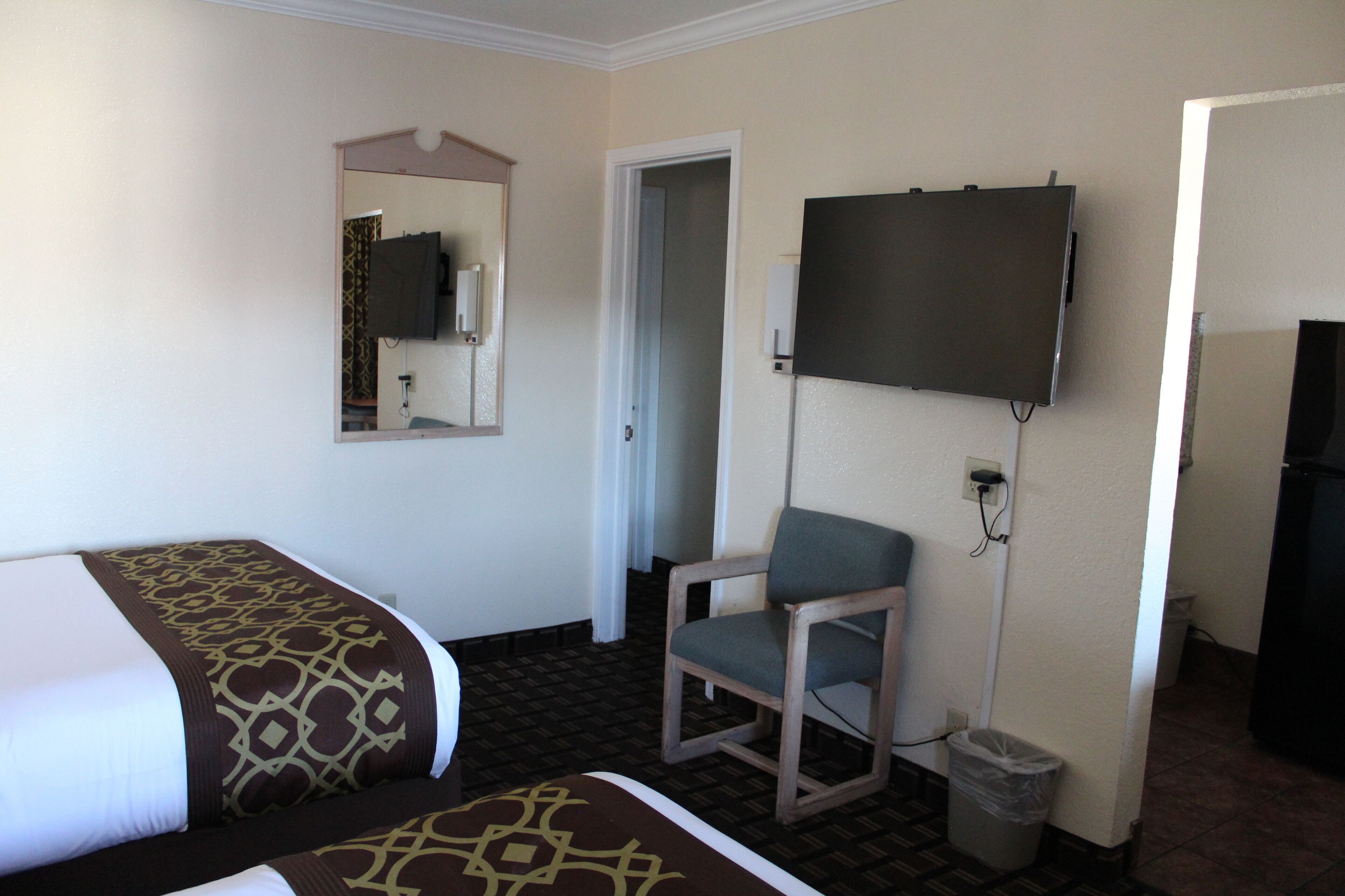 A hotel room with a bed, a chair, a television, and a trash can.