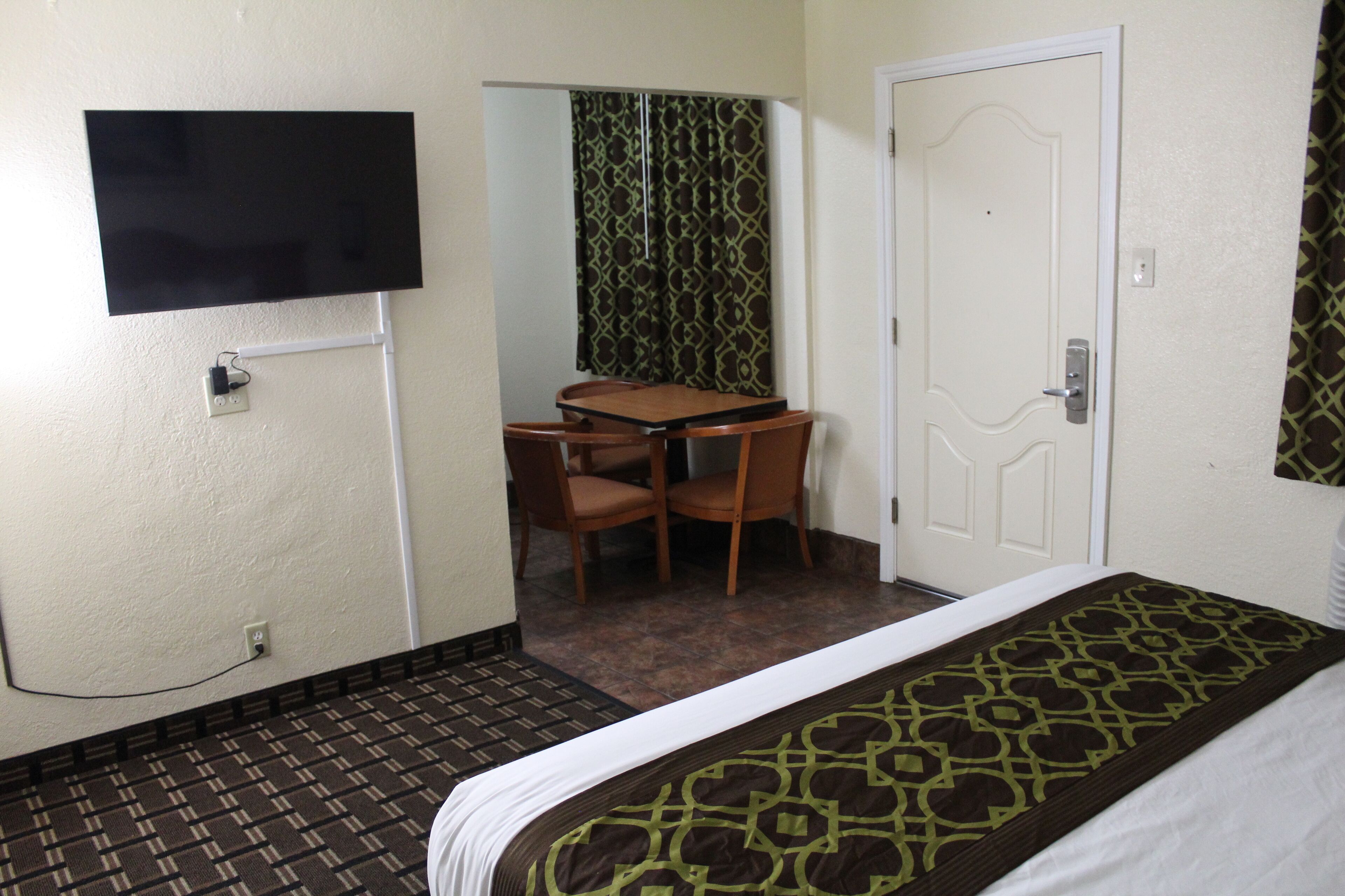 Une chambre d’hôtel comprenant un lit, un bureau avec des chaises, une télévision et une porte.