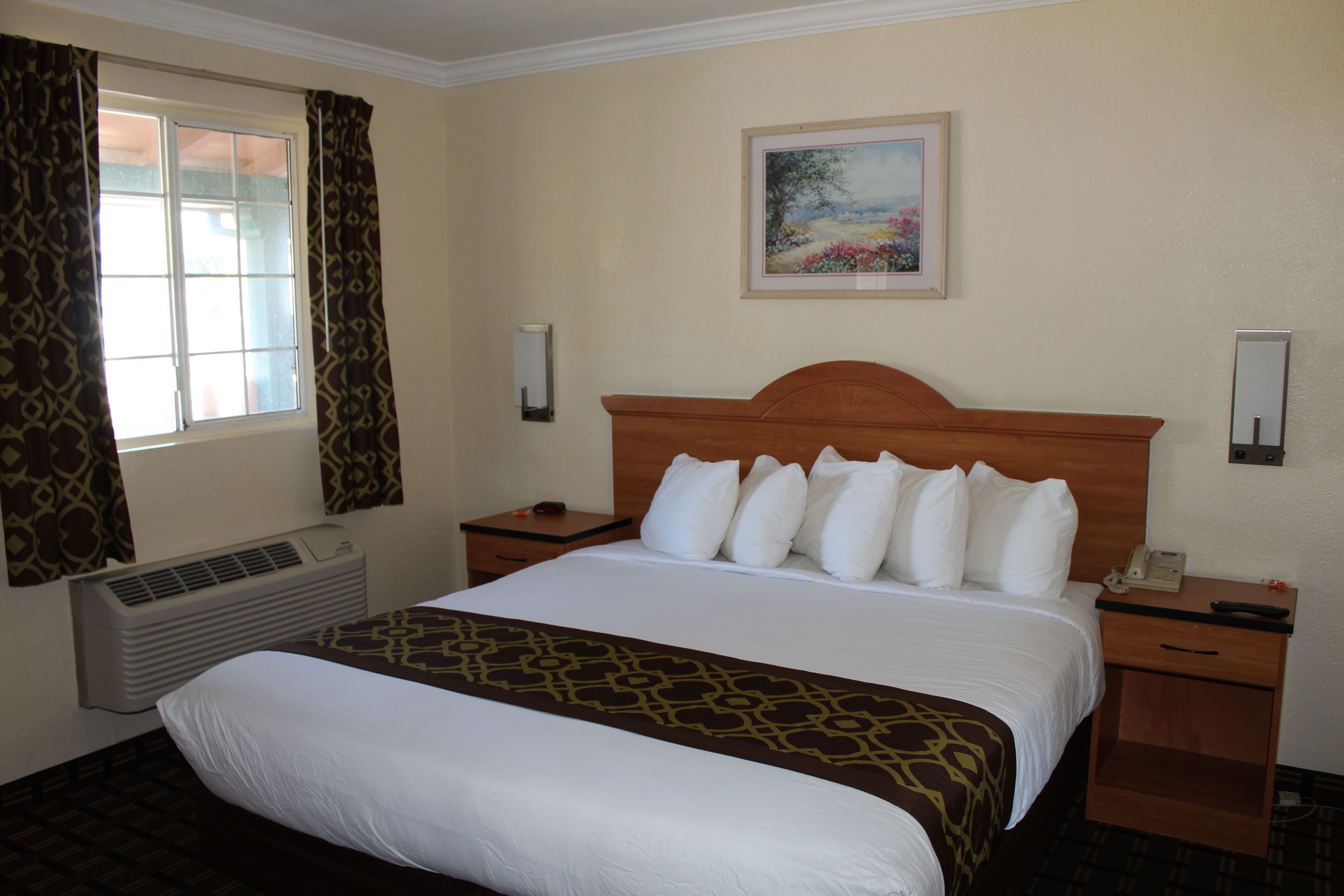 A hotel room with a large bed, a nightstand, a bedside table, a wall-mounted telephone, and a painting above the bed.