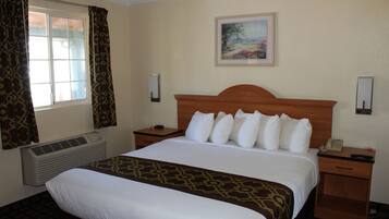A hotel room with a large bed, a nightstand, a bedside table, a wall-mounted telephone, and a painting above the bed.