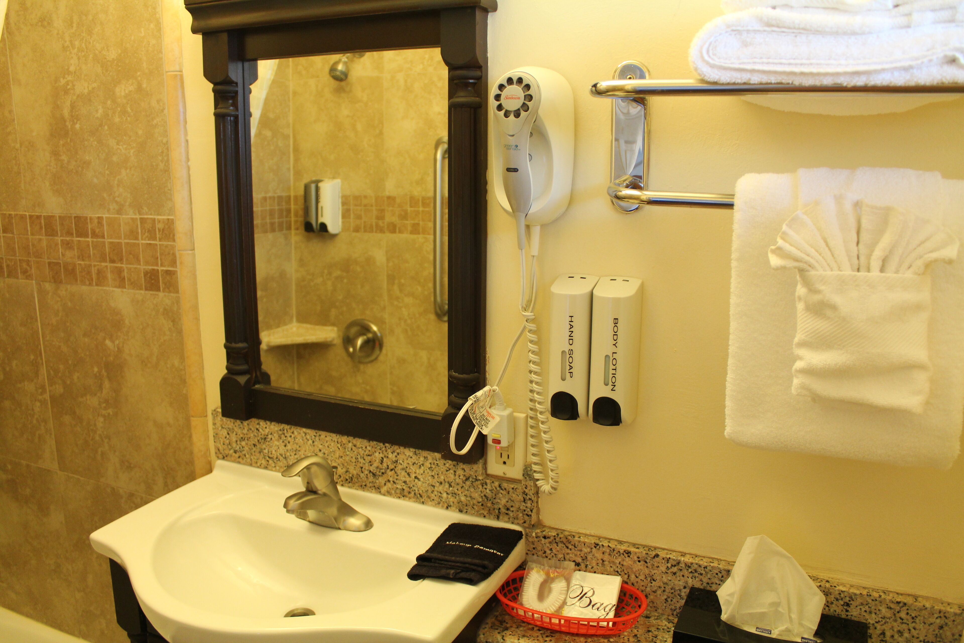 Un baño con lavamanos, secador de pelo, toallero y artículos de aseo.