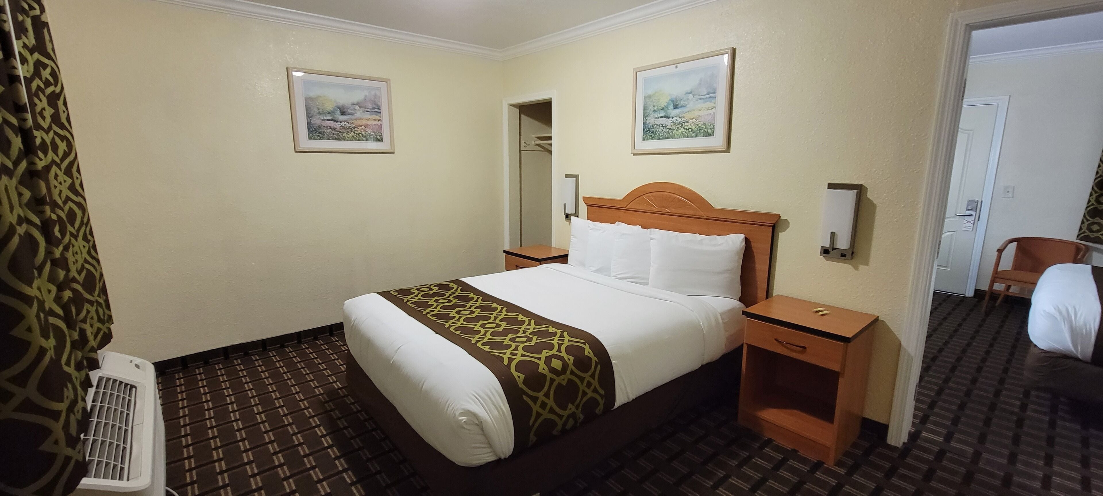 Hotelkamer met een bed, nachtkastje, verwarming, spiegel en twee ingelijste foto’s aan de muur.