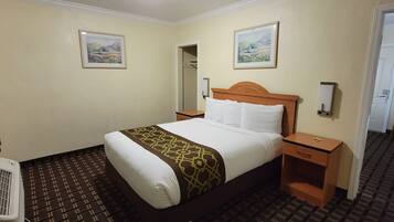 Hotelkamer met een bed, nachtkastje, verwarming, spiegel en twee ingelijste foto’s aan de muur.