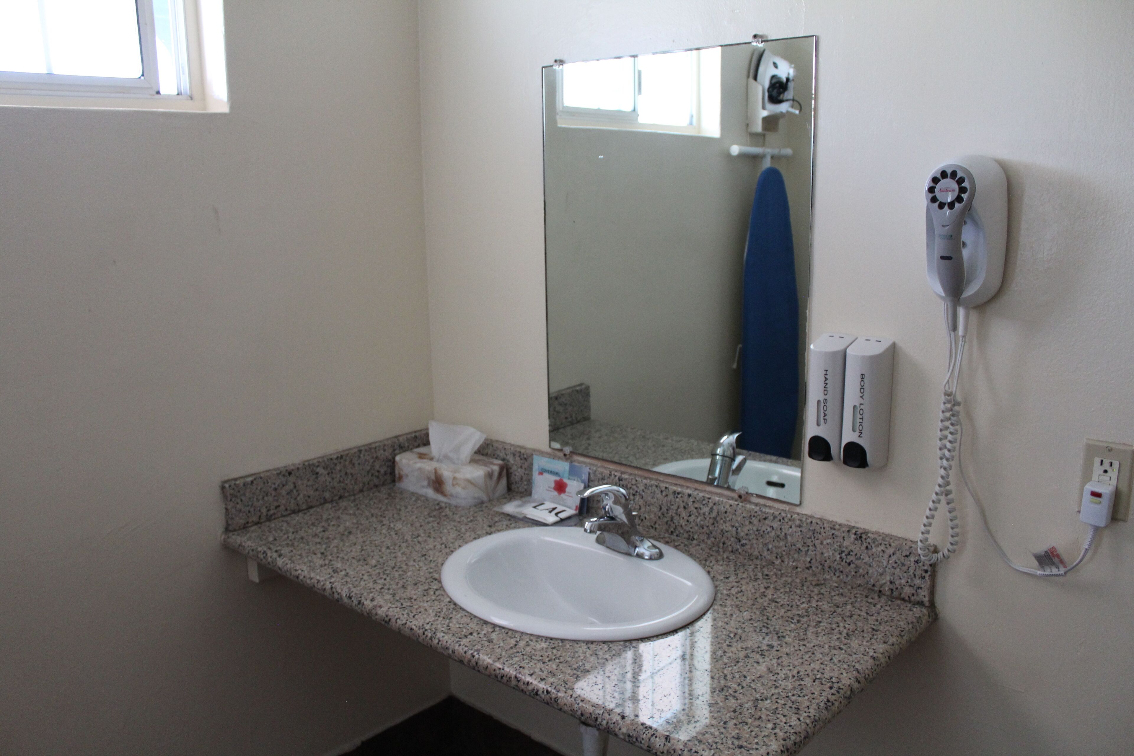 A bathroom with a granite countertop, a white sink, a mirror, a hairdryer, and a towel rack.