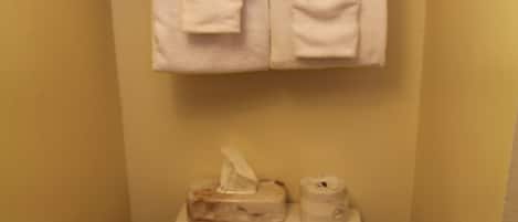 A small bathroom with a toilet, a stack of white towels, a tissue box, and a toilet paper holder.
