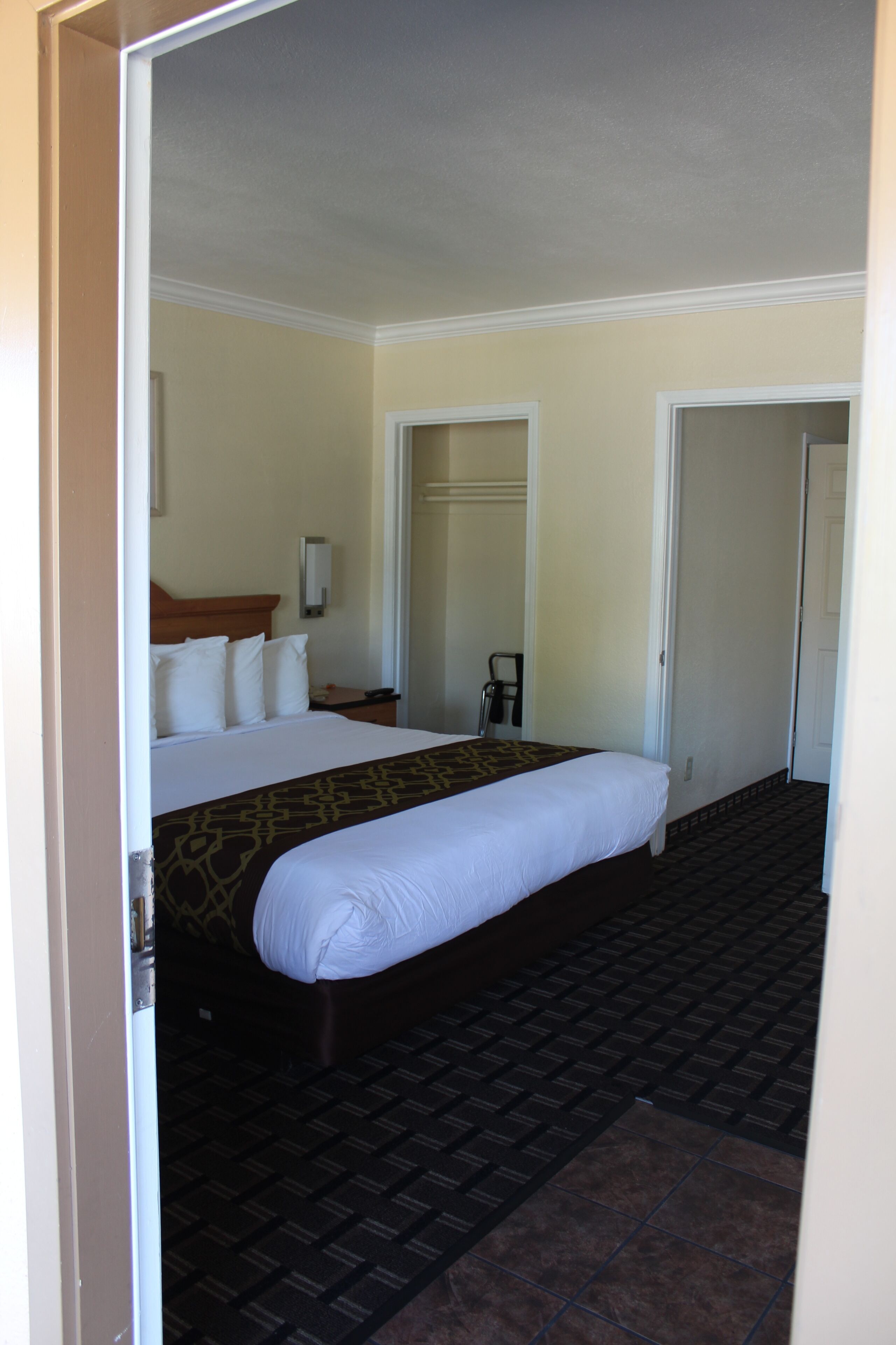 A hotel room with a large bed, a bedside table, a chair, and a door.