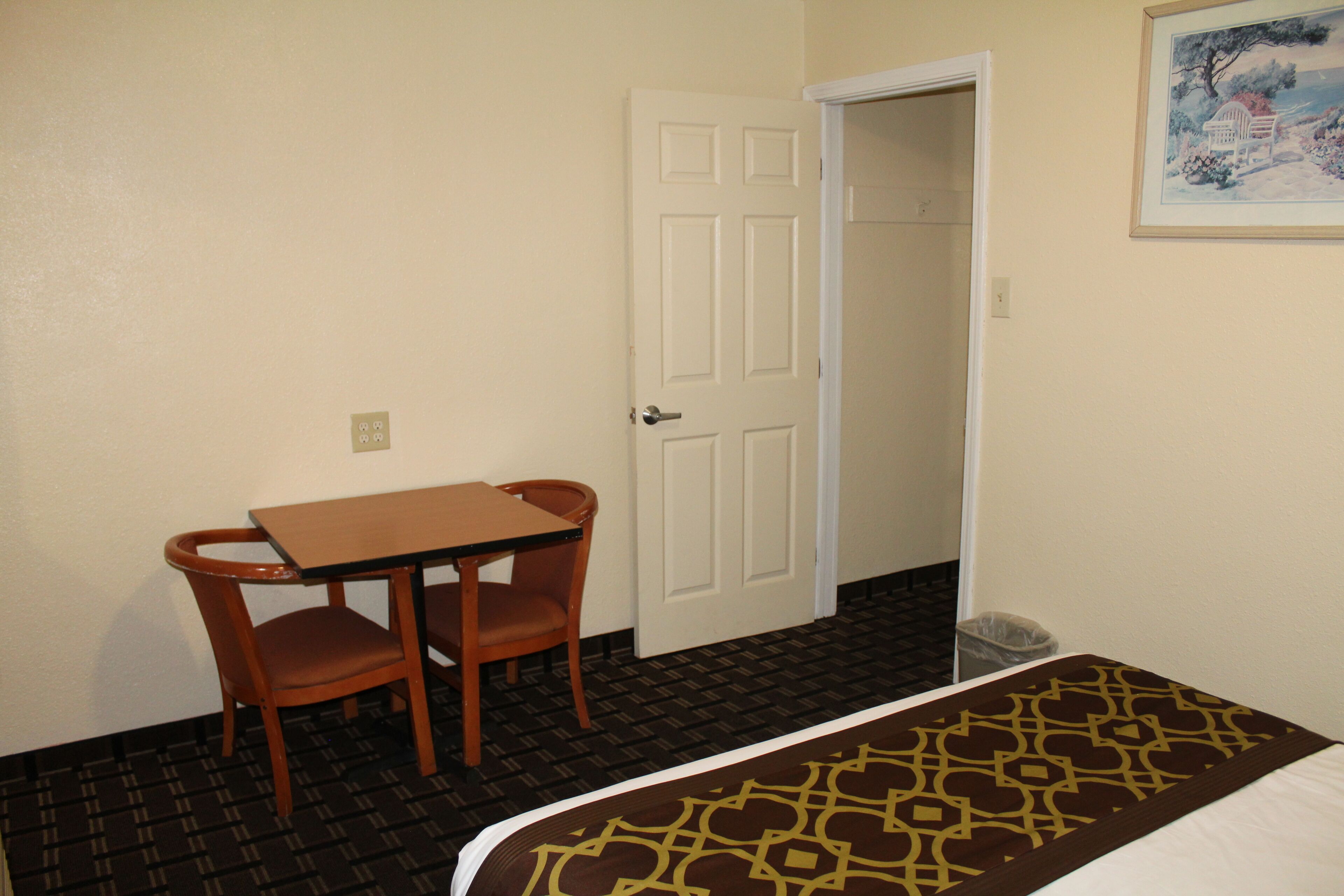 A hotel room with a bed, a table, two chairs, a door, and a painting on the wall.