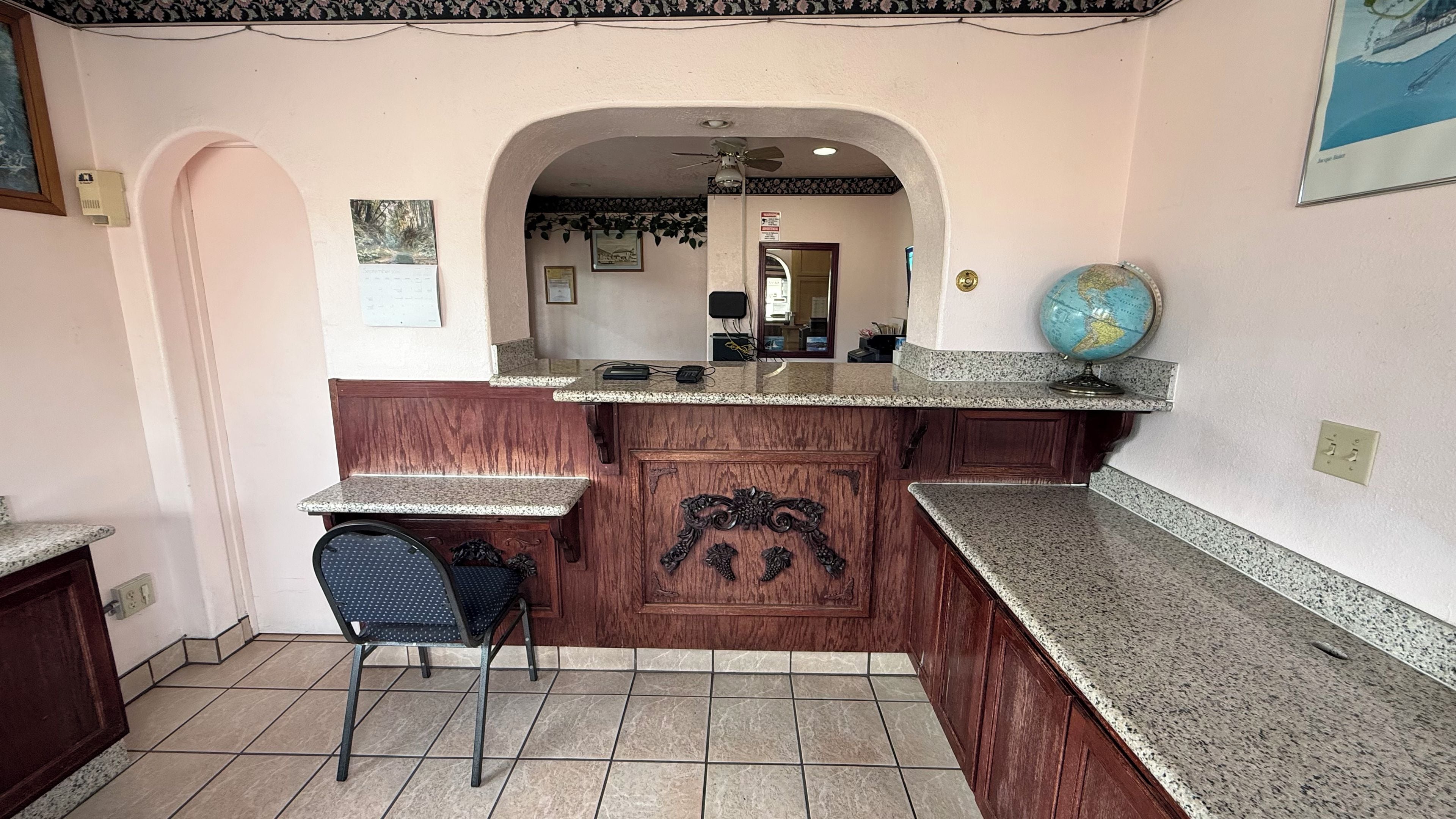 A kitchen with a marble countertop, a wooden cabinet with a decorative handle, a chair, and a globe on the counter.