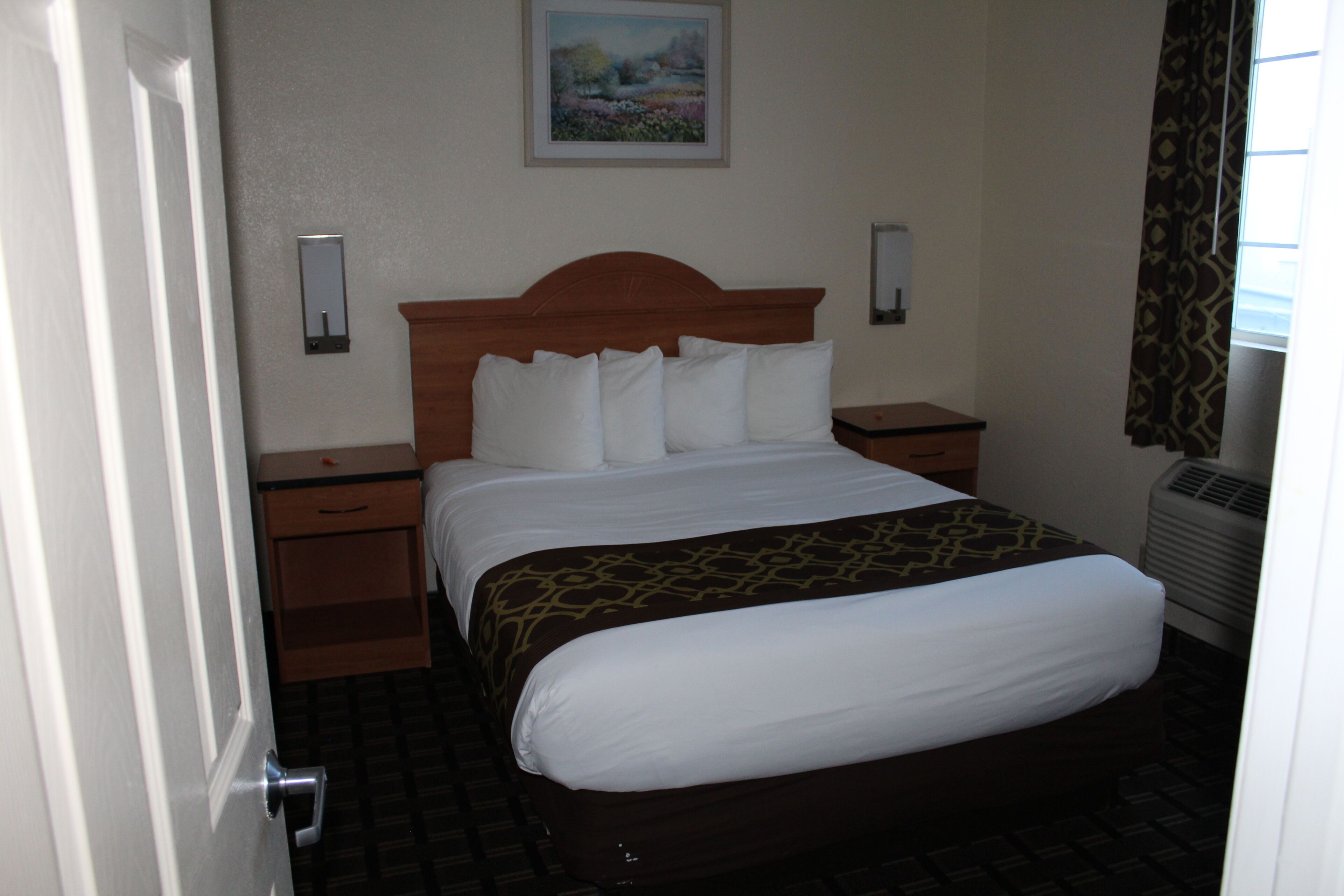 Habitación de hotel con cama, mesitas de noche, lámpara de pared, un cuadro y equipo de aire acondicionado.