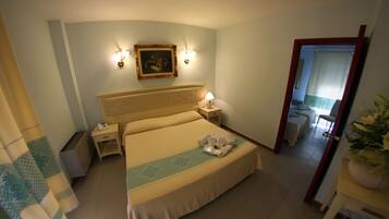 Habitación de hotel con cama, mesitas de noche, una lámpara, un cuadro en la pared y una planta en maceta.