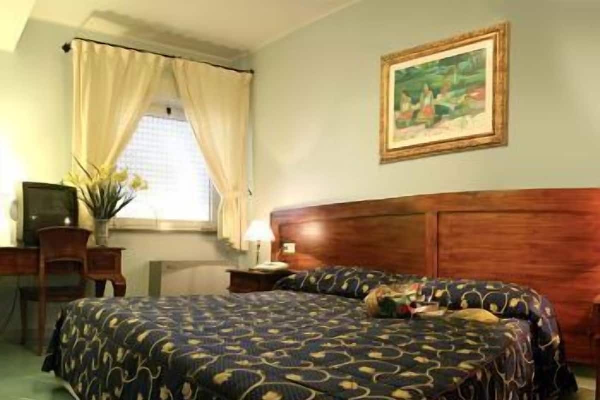 Un cuarto de hotel con una cama grande, cabecera de madera, un escritorio con lámpara y un cuadro en la pared.
