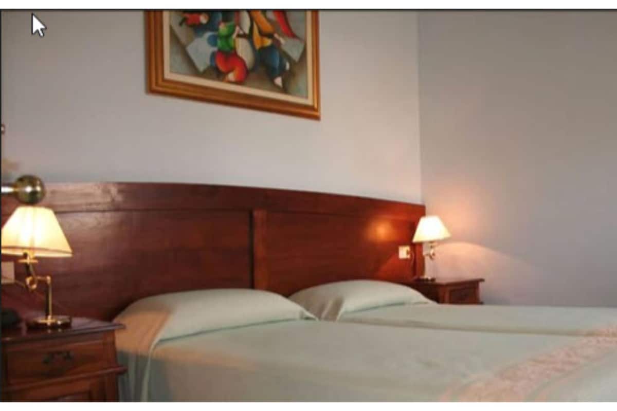 Una habitación de hotel con cabecera de madera, dos camas, lámparas de noche y un cuadro en la pared.