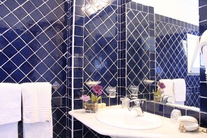 A bathroom with a white sink, a mirror, and blue-tiled walls. - Hotel Marini (Sassari)