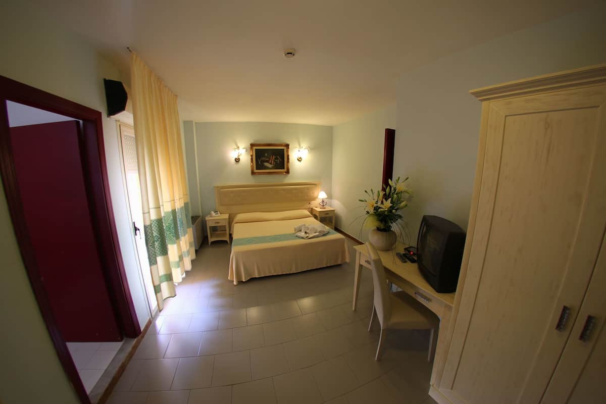 Una habitación de hotel con una cama, mesitas de noche, un escritorio con televisor y un armario.