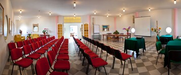 Un salón de conferencias con filas de sillas rojas, una mesa con mantel verde y una pizarra.