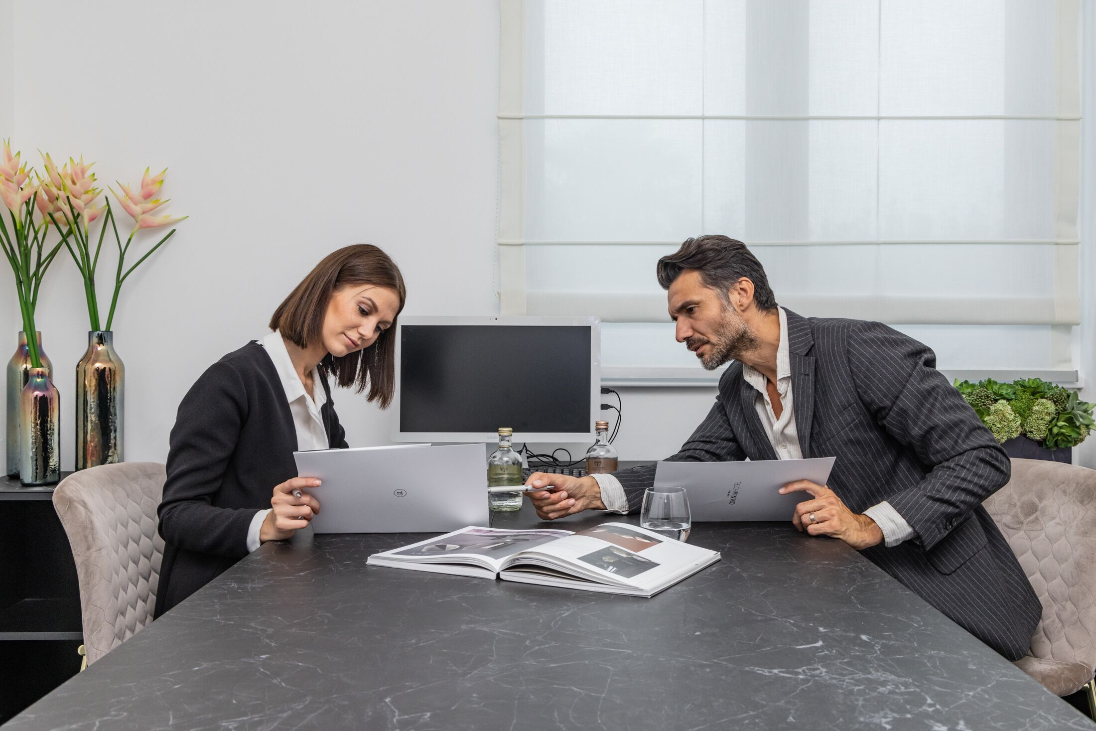 Two people at a table with a laptop, a book, and a glass of water.