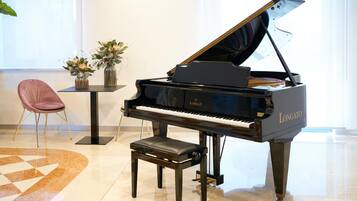 A grand piano in a well-lit room with a marble floor, a pink chair, and a small table with vases.