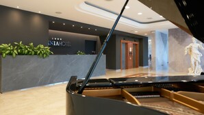 A grand piano in a hotel lobby with a reception desk and a statue in the background.