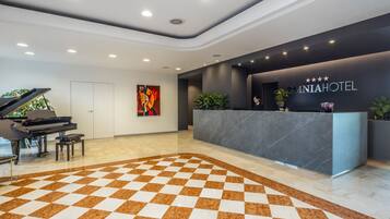 A hotel reception area with a checkered floor, a reception desk, a piano, and a painting on the wall.