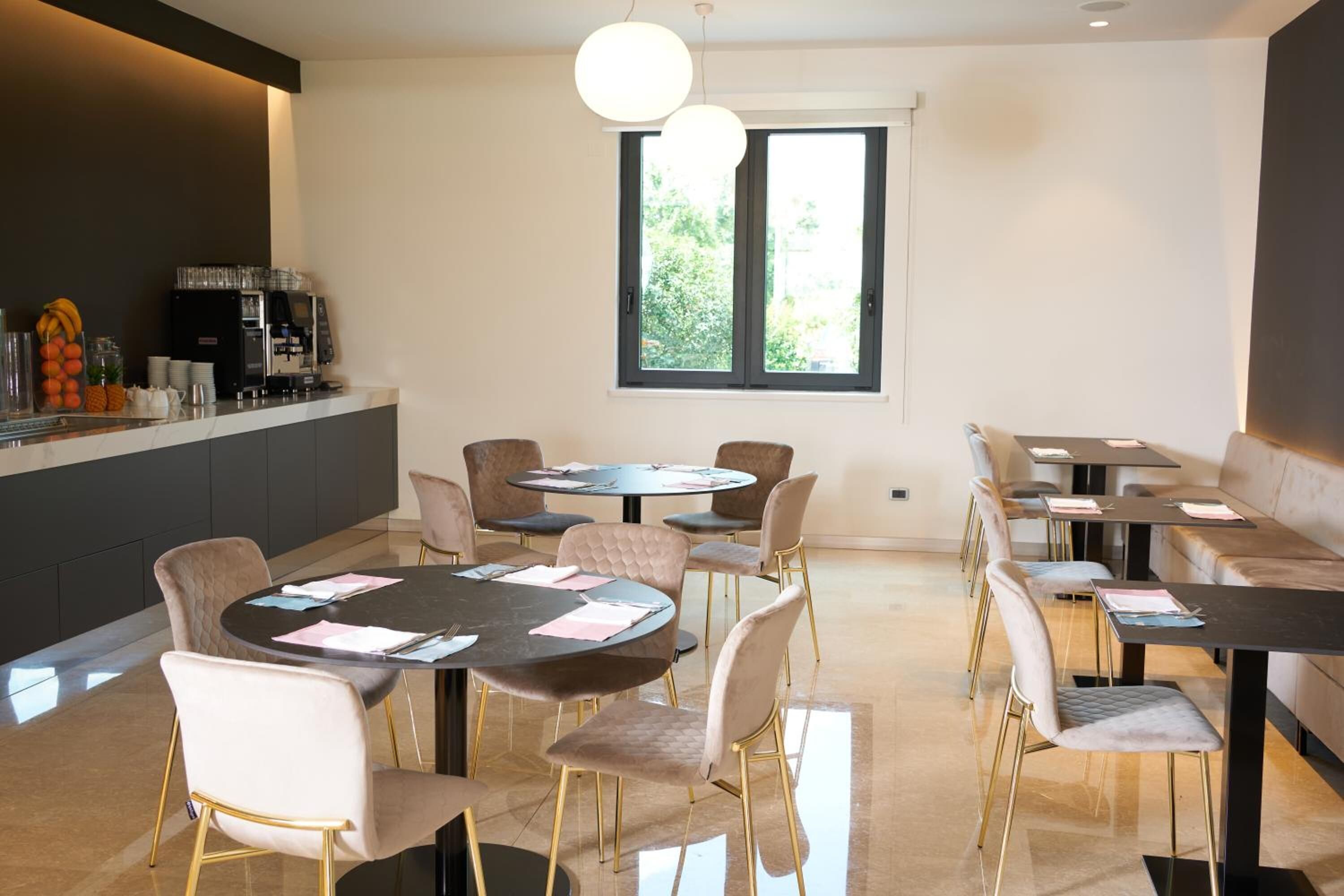 Un comedor moderno con mesas redondas y sillas acolchadas, una cafetera y vistas a zonas verdes por una ventana.