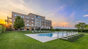 A hotel with a swimming pool, sun loungers, and a well-maintained lawn.