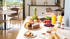 A breakfast table with various fruits, pastries, and beverages, set in a modern dining area with a view of a pool.