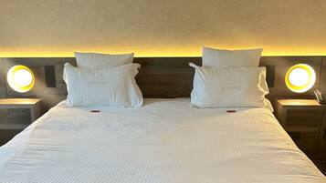 Een netjes opgemaakt bed met witte lakens en kussens, twee nachtkastjes met verlichte lampen, en een houten hoofdeinde.