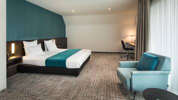 A hotel room with a large bed, a desk, a chair, and a small table.