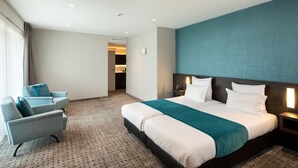Habitación de hotel con una cama grande, una zona de estar con dos sillones, suelo alfombrado y vistas a un pasillo.
