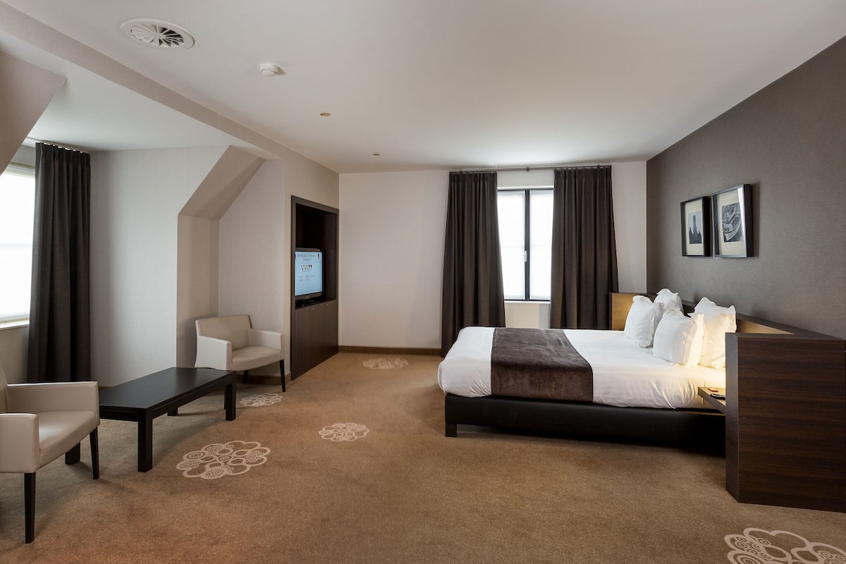 Una habitación de hotel con una cama, dos sillas, un televisor y un escritorio.
