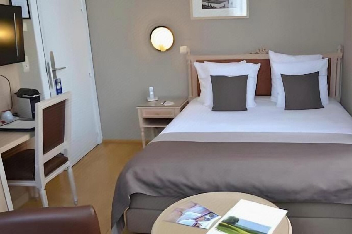 A hotel room with a bed, bedside table, chair, and a small table with a magazine.