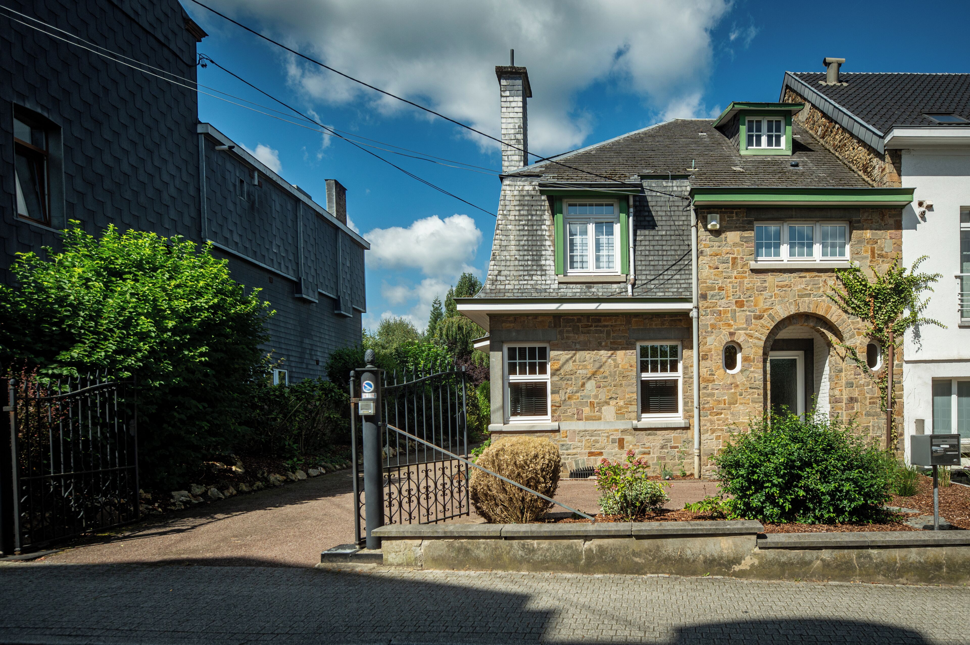 A two-story stone house with a stone chimney, a small attached garage, and a paved driveway.