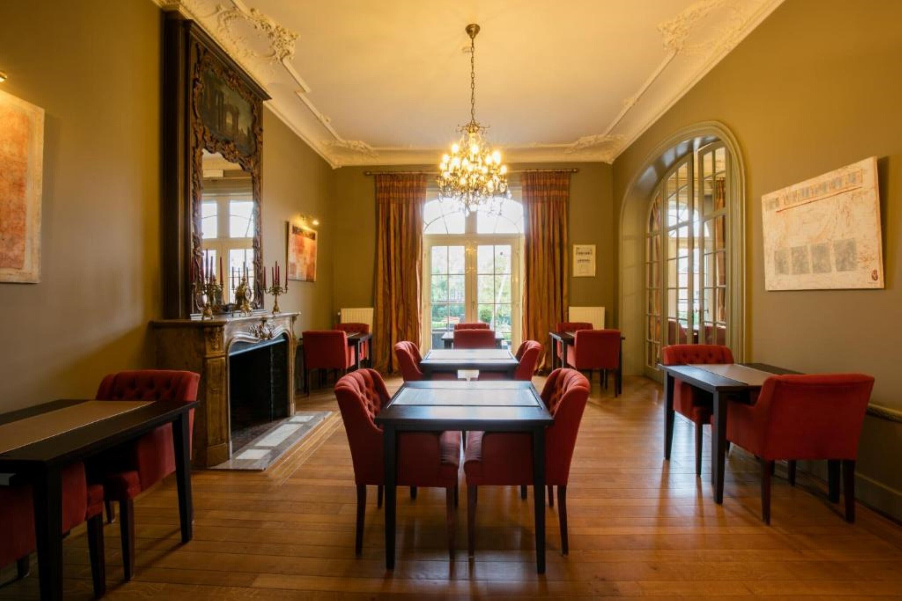 A dining area with a chandelier, red upholstered chairs, and a fireplace.