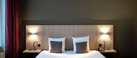 Una cama bien hecha con dos almohadas, una mesita de noche con lámpara y un aplique en la pared.
