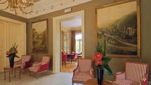 A spacious lobby with striped armchairs, a chandelier, and large landscape paintings on the walls.