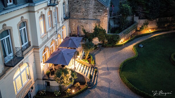 A courtyard with a stone building, a paved walkway, and outdoor seating with umbrellas.