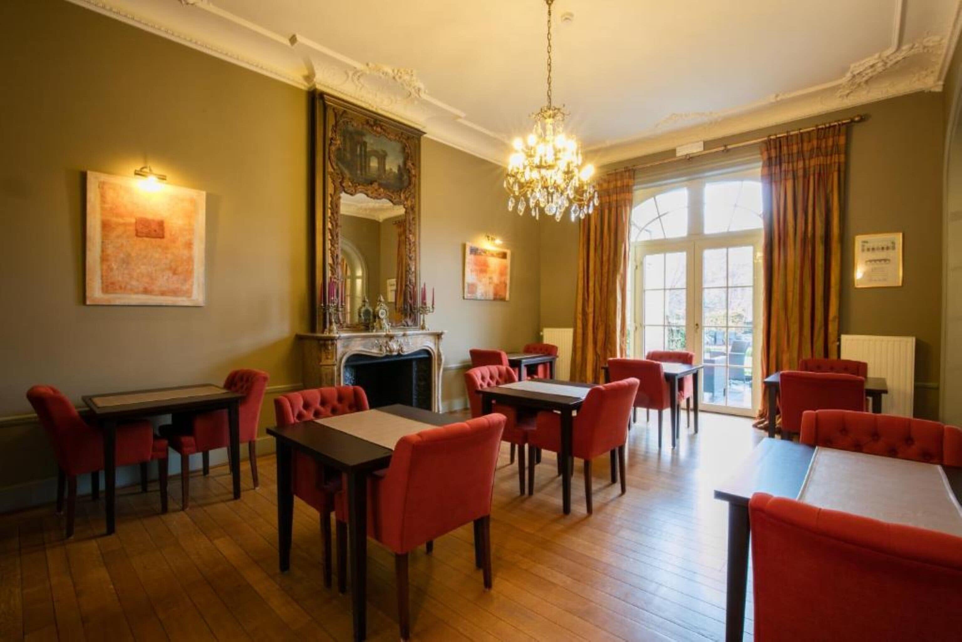 A dining area with red upholstered chairs and tables, a chandelier, and a fireplace.
