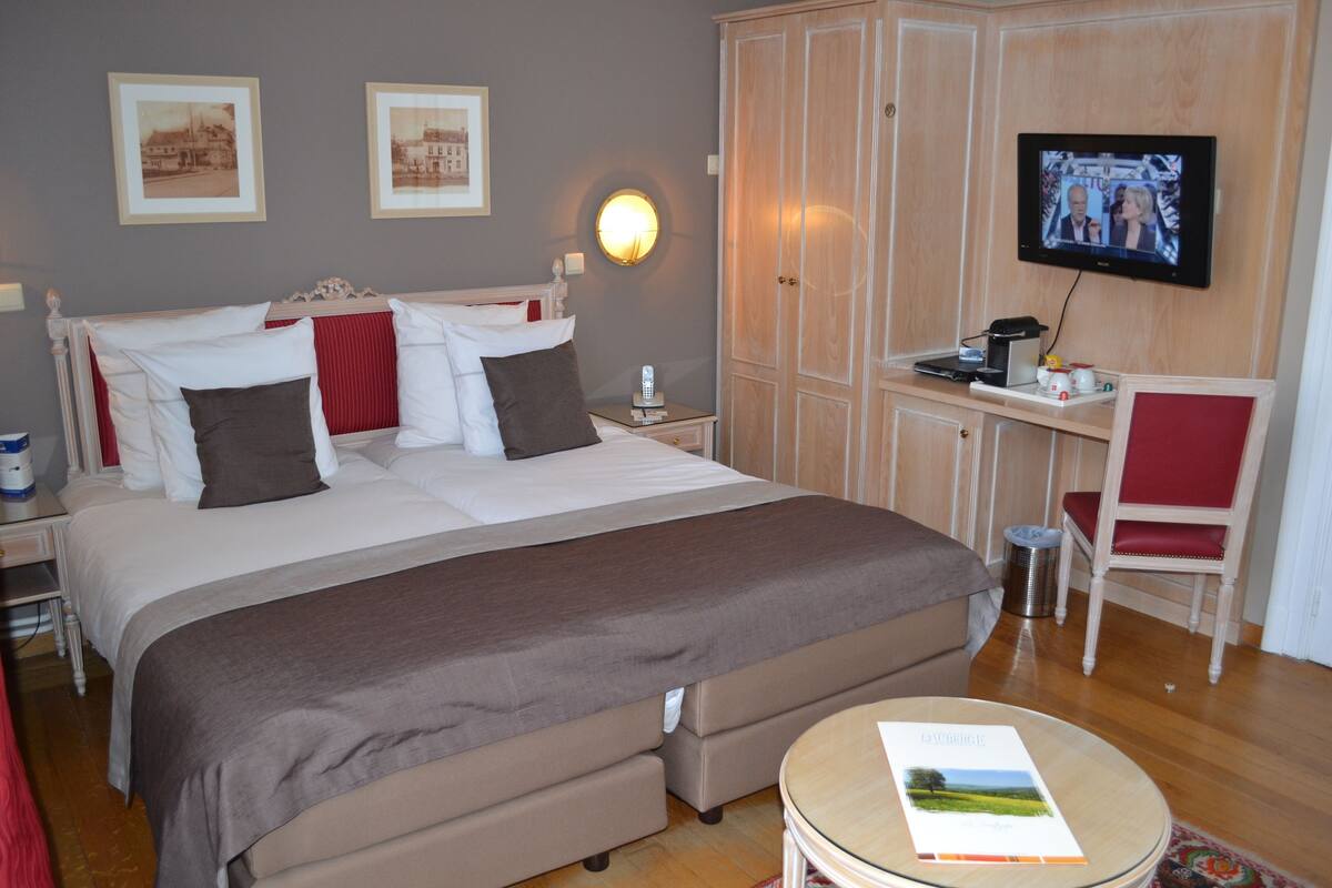 A hotel room with a bed, a desk, a chair, a television, and framed pictures on the wall.