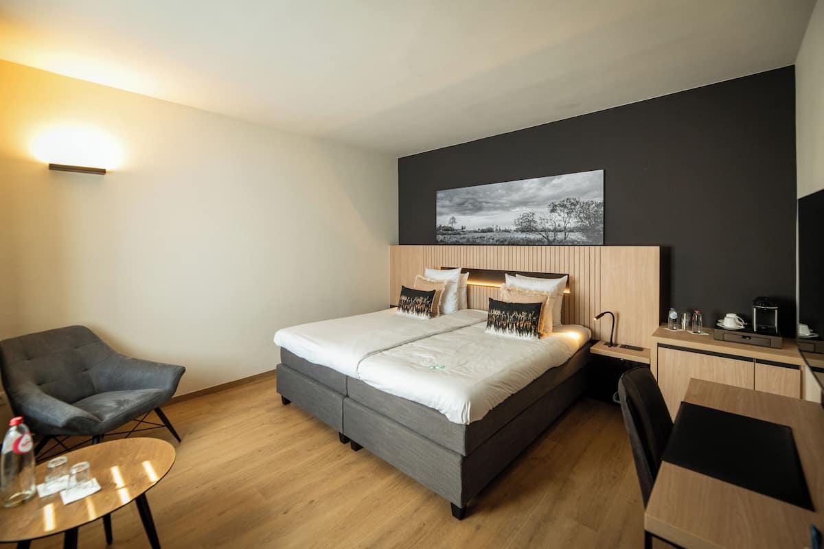 A modern hotel room with a bed, a desk, a chair, and a small table.