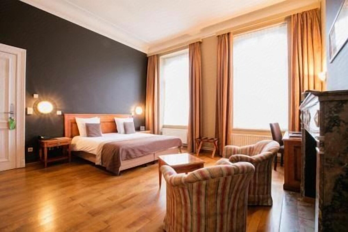 A hotel room with a bed, two bedside tables, a chair, a desk, and a fireplace.