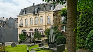 A courtyard with outdoor seating, a stone building with a balcony, and a tree.