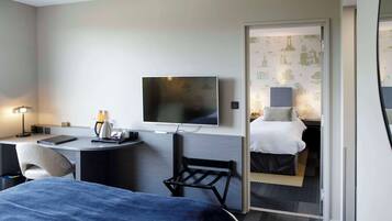 A hotel room with a bed, desk, chair, TV, and a separate bedroom with a bed and nightstand.