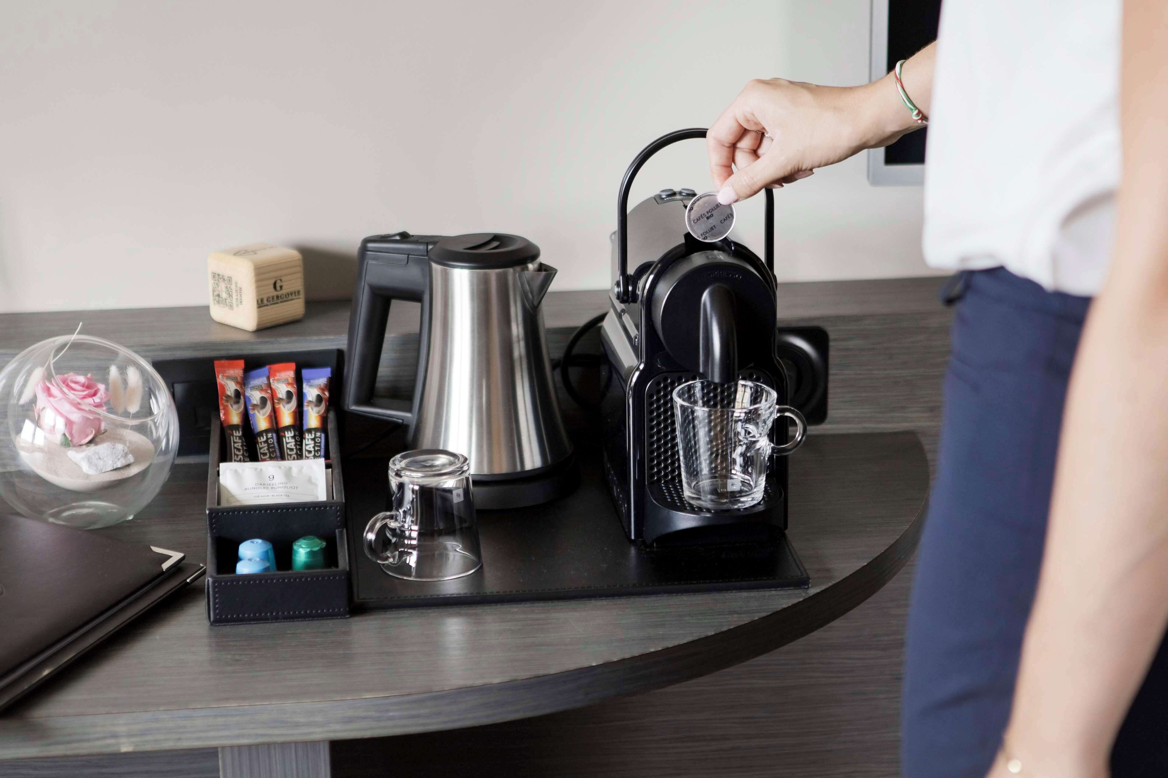 A coffee machine, a kettle, a glass, and a box of coffee pods on a countertop.