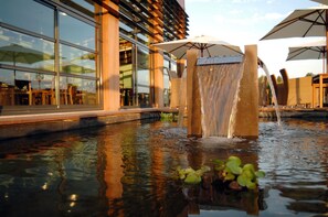 A water feature with a cascading waterfall in front of a building with large windows and outdoor seating. - Best Western Plus Hotel Gergovie (Perignat-les-Sarlieve)