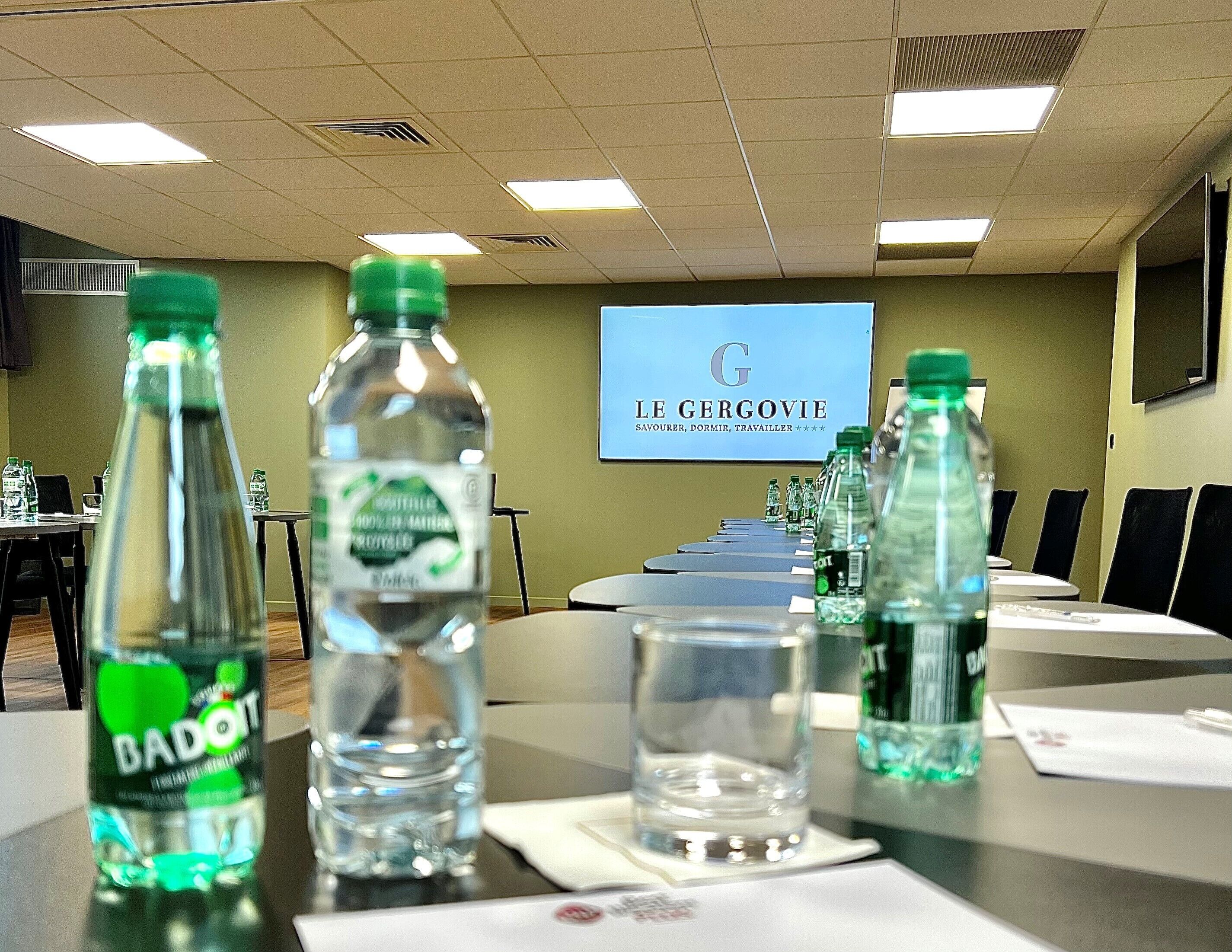 A conference room with tables, chairs, water bottles, and a projector screen displaying "LE GERCOVIE".