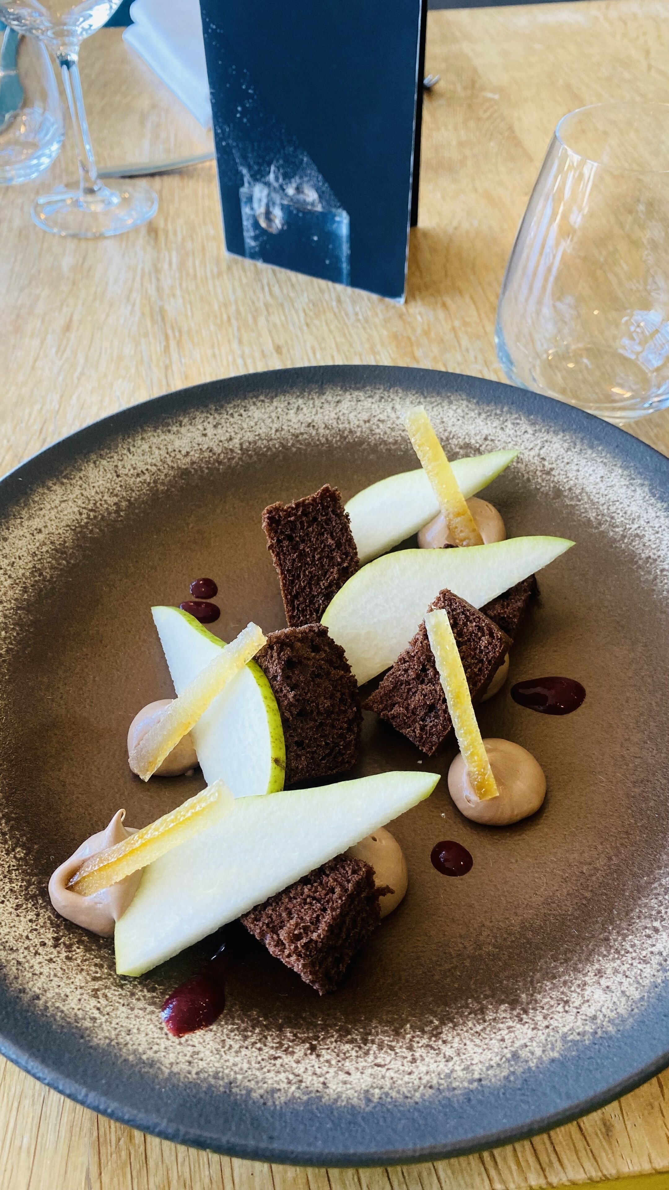 A dessert plate with chocolate pieces, apple slices, and a creamy sauce on a textured plate.