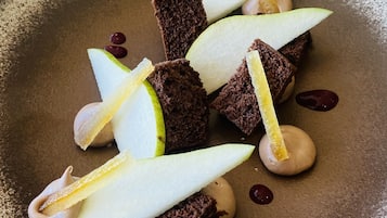 A dessert plate with chocolate pieces, apple slices, and a creamy sauce on a textured plate.