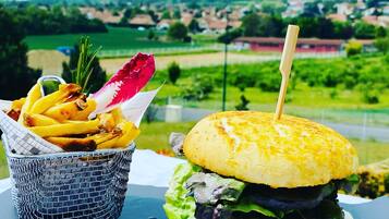 Un hamburger et des frites sur une table, avec une vue panoramique sur un paysage verdoyant et des collines en arrière-plan.
